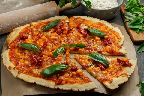 Eine Pizza mit Kürbis, Tomatensauce und Basilikum belegt auf einem Holzbrett