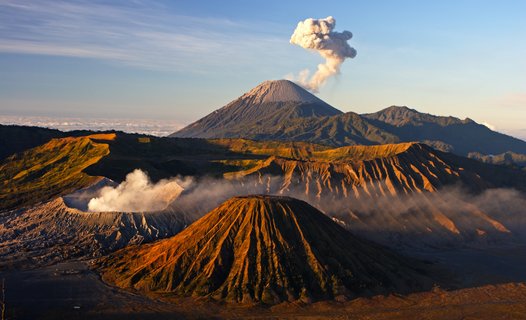 Panorama mit Blick über die karge Landschaft auf einen rauchenden Vulkan