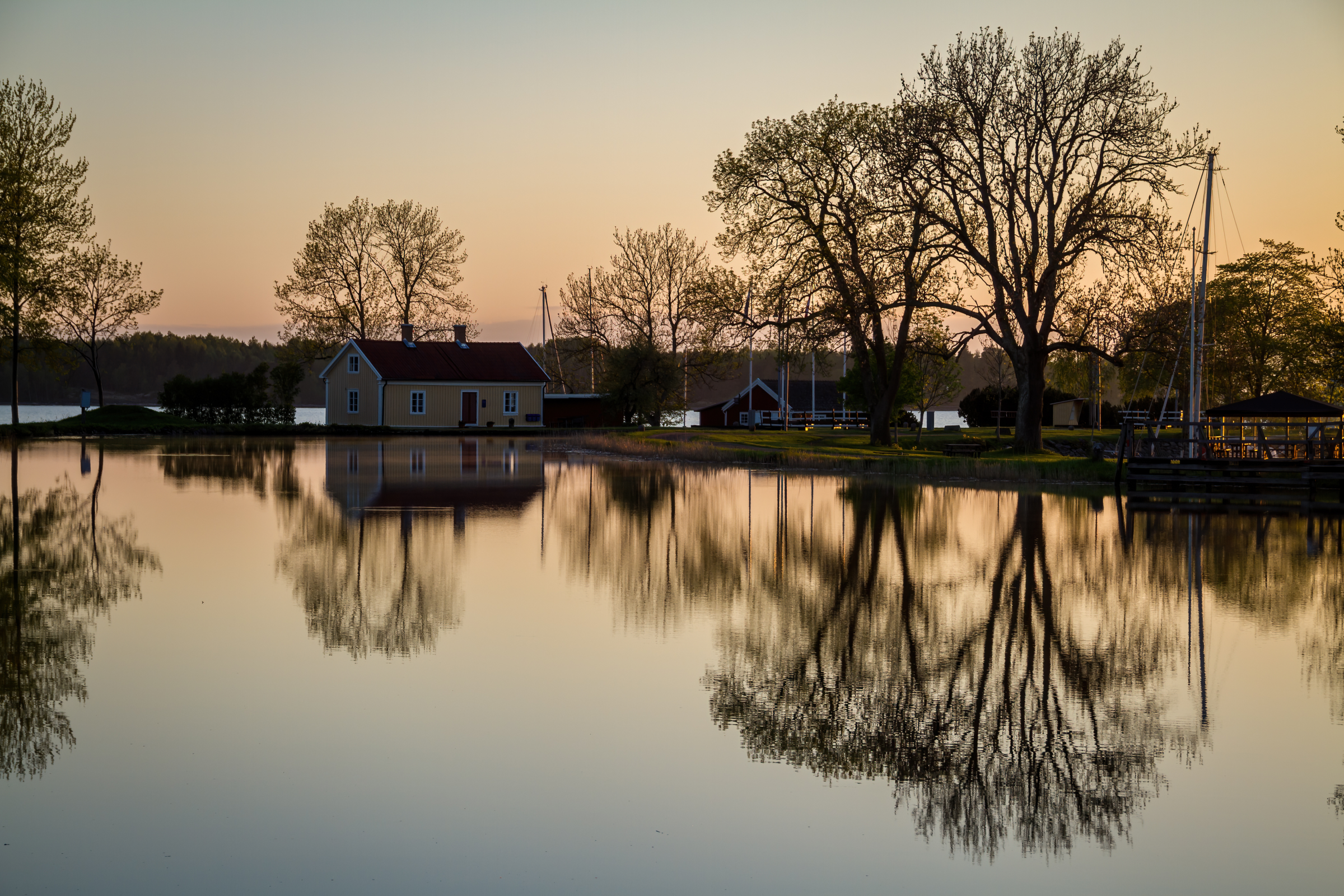 Die untere Bildhälfte wird von einer spiegelnden Wasserfläche eingenommen, die die dahinterliegenden Bäume sowie ein gelbes Haus reflektiert.