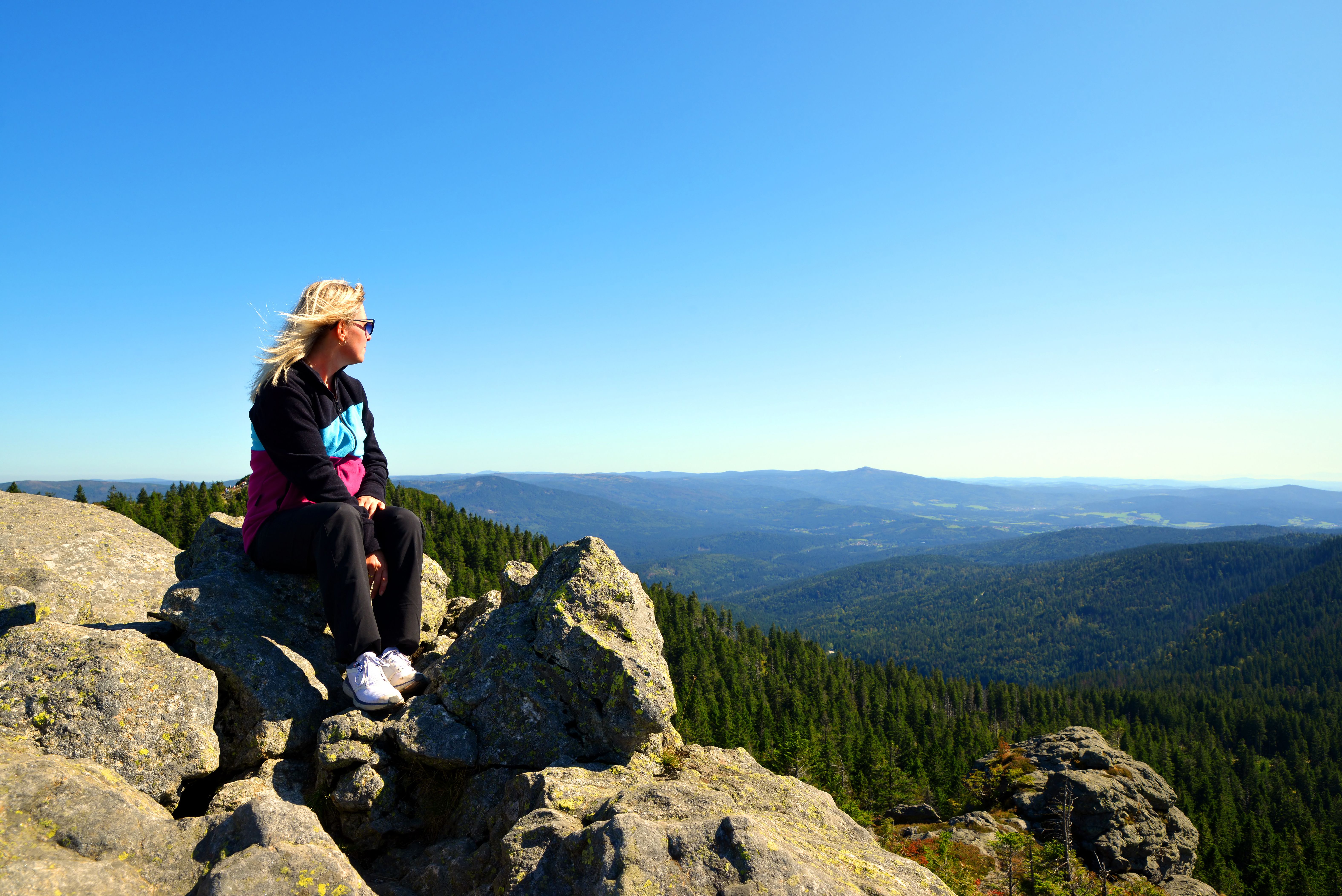 Frau sitzt auf dem Gipfel des Großen Arber im Bayerischer Wald und genießt den Blick in die Ferne
