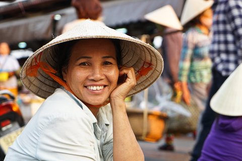 Vietnamesin mit Kegelhut lächelt auf einem Markt in die Kamera.