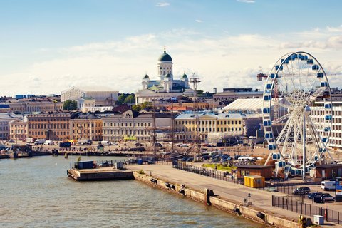Vom Wasser im Hafen aus blickt man auf die Skyline Helsinkis. Zentral hinten im bild befindet sich der weiße Dom, rechts im Vordergrund steht ein Riesenrad.