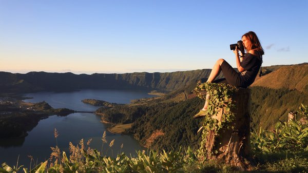 Eine Frau auf dem Berggipfel macht bei Dämmerung ein Foto mit ihrer Kamera