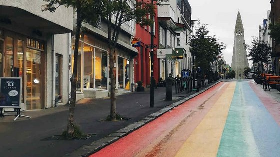 Regenbogenstraße in Reykjavík mit Blick auf Hallgrímskirkja Eine bunte Straße in Regenbogenfarben führt durch ein Wohn- und Geschäftsviertel in Reykjavík. Am Ende der Straße erhebt sich die moderne Kirche Hallgrímskirkja.