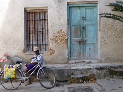Ein Mann sitz mit seinem Fahrrad vor einem Haus in Stone Town auf Sansibar.