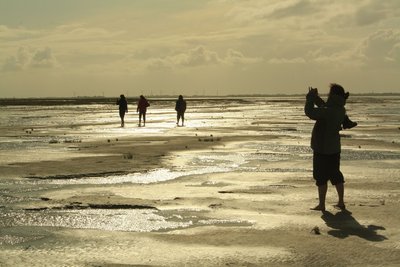 Eine Frau fotografiert den Sonnenuntergang über dem Wattenmeer.