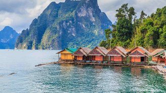 See mit aneinandergereihten roten Bungalows und grünem Berg im Hintergrund