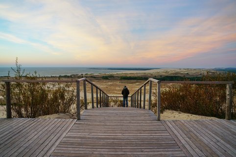 Ein Reisender schaut von einer Holzplattform aus über die Dünen der Kurischen Nehrung