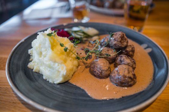 Auf einem schwarzen Teller liegen einige Fleischklößchen in Sauce mit einem Klacks Kartoffelpüree.