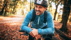 Ein Radfahrer steht im Wald und lächelt in die Kamera