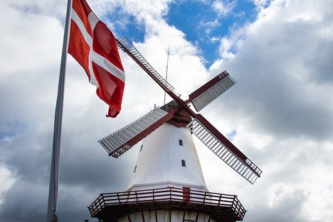 Bild einer weißen Mühle, das nach oben fotografiert wurde. Davor weht die rot-weiße Dänemark-Flagge.