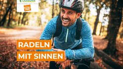 Radeln mit Sinnen Ein Radfahrer steht im Wald und lächelt in die Kamera