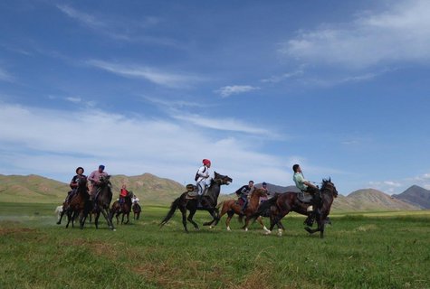 Eine Gruppe von Kirgisen reitet über eine Wiese