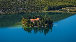 Das Krka-Kloster im Krka-Nationalpark, Kroatien, liegt malerisch am Fluss. Umgeben von grüner Natur spiegelt sich das historische Gebäude im Wasser und strahlt eine besondere Ruhe aus.