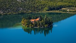 Krka-Kloster – Spirituelle Oase im Nationalpark Das Krka-Kloster im Krka-Nationalpark, Kroatien, liegt malerisch am Fluss. Umgeben von grüner Natur spiegelt sich das historische Gebäude im Wasser und strahlt eine besondere Ruhe aus.