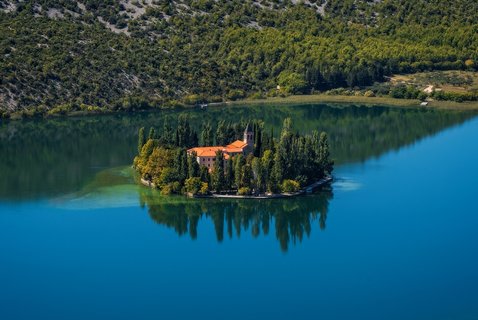 Das Krka-Kloster im Krka-Nationalpark, Kroatien, liegt malerisch am Fluss. Umgeben von grüner Natur spiegelt sich das historische Gebäude im Wasser und strahlt eine besondere Ruhe aus.