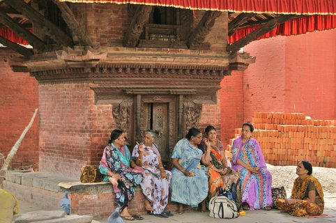 Einheimische Frauen sitzen an einem Steingebäude und Unterhalten sich