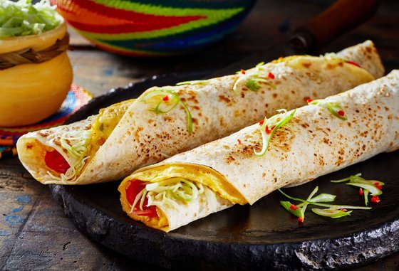 Ein frisch zubereitetes Ugandisches Rolex, ein beliebtes Streetfood bestehend aus einem Chapati-Fladen, gefüllt mit Eiern und Gemüse, auf einem Holztisch serviert.