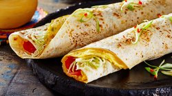 Ein frisch zubereitetes Ugandisches Rolex, ein beliebtes Streetfood bestehend aus einem Chapati-Fladen, gefüllt mit Eiern und Gemüse, auf einem Holztisch serviert.