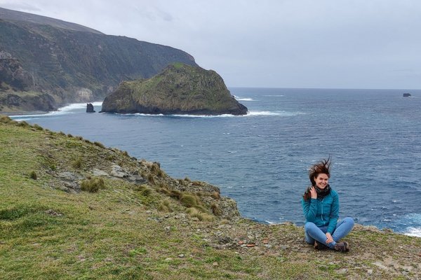 Ina Fick steht auf einem grünen Hügel mit Blick auf die hügelige Vulkanlandschaft der Azoren – umgeben von saftigem Gras und fernab touristischer Pfade.