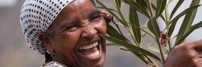 Herzliche Einheimische auf den Kapverden Lachende Frau mit weiß-schwarz gepunktetem Kopftuch hält einen Oleander-Zweig auf den Kapverden.