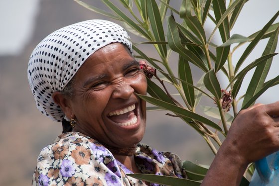 Herzliche Einheimische auf den Kapverden Lachende Frau mit weiß-schwarz gepunktetem Kopftuch hält einen Oleander-Zweig auf den Kapverden.