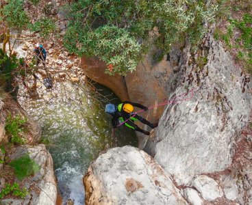 Was für Abenteuerlustige: Canyoning Ein Mann in Neoprenanzug und Sturzhelm seilt sich von einem Felsen in ein Gewässer ab.