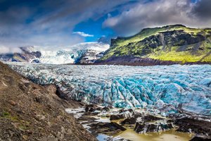 Der Vatnajökull kalbt in den See Jökulsárlón Eine blau schimmernde Gletscherzunge schiebt sich durch eine felsige Landschaft.