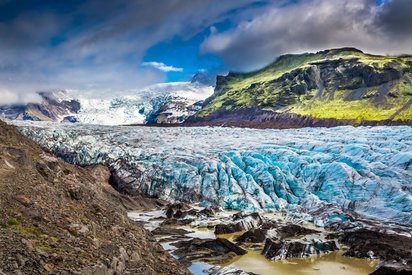 Der Vatnajökull kalbt in den See Jökulsárlón Eine blau schimmernde Gletscherzunge schiebt sich durch eine felsige Landschaft.