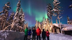 Eine Gruppe Menschen schaut sich in einer Winterlandschaft Polarlichter an