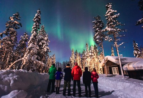 Eine Gruppe Menschen schaut sich in einer Winterlandschaft Polarlichter an