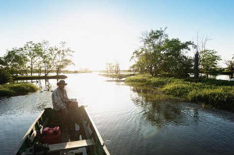 Mann sitzt bei Sonnenaufgang im Boot auf dem Fluss