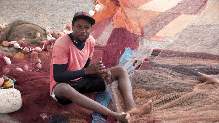 Junger Kapverdianer sitzt auf dem Boden und knüpft Fischernetze.
