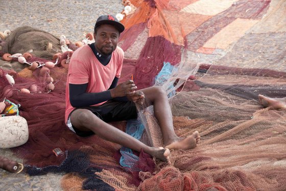 Junger Kapverdianer sitzt auf dem Boden und knüpft Fischernetze.