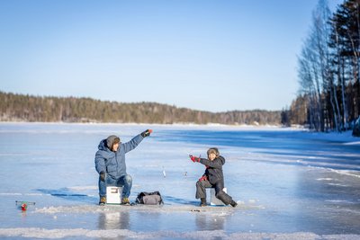 Auf einer weiten Eisfläche angeln ein Erwachsener und ein Kind.