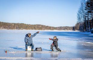 Eisfischen gehört in Finnland zu den traditionsreichen Winteraktivitäten Auf einer weiten Eisfläche angeln ein Erwachsener und ein Kind.
