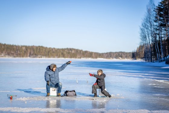 Eisfischen gehört in Finnland zu den traditionsreichen Winteraktivitäten Auf einer weiten Eisfläche angeln ein Erwachsener und ein Kind.