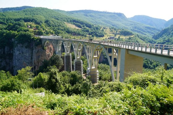 Von hinten links nach vorne rechts führt eine lange, weiße Brücke durch eine bewaldete Schlucht.