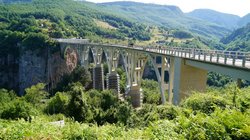 Von hinten links nach vorne rechts führt eine lange, weiße Brücke durch eine bewaldete Schlucht.