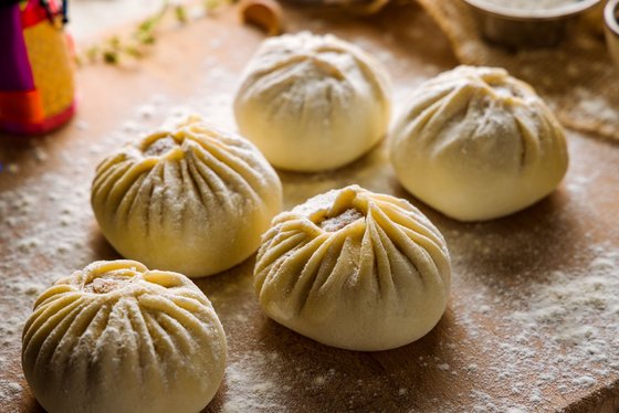 Traditionelle mongolische Teigtaschen (Buuz) Ein Teller mit gedämpften mongolischen Teigtaschen (Buuz), garniert mit frischen Kräutern, präsentiert auf einem rustikalen Holztisch.