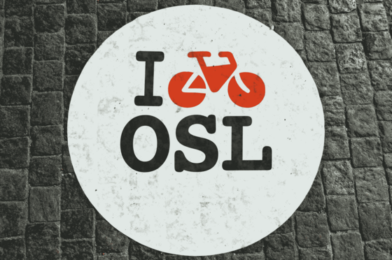 Auf dem grauen Asphalt ist ein weißer Kreis mit einem Schriftzug bestehend aus dem englischen Wort I, einem Fahrrad und OSL.