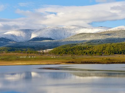 Das untere Bilddrittel wird von einer Wasserfläche eingenommen, am dahinterliegenden Ufer befindet sich eine weite Wiese, auf der links der Bildmitte ein paar weiße Jurten stehen. Die obere Bildhälfte wird von einem bergigen Waldgebiet eingenommen, das mit der Höhe immer verschneiter wird. Das oberste Bilddrittel besteht nur noch aus blauem Himmel, der aber größtenteils von einer weißen Wolkendecke bedeckt ist.
