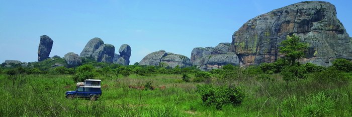 Safarifahrzeug in grün bewachsener Landschaft mit schwarzen Felsen im Hintergrund in Angola.