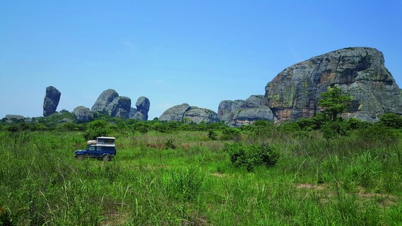Safarifahrzeug in grün bewachsener Landschaft mit schwarzen Felsen im Hintergrund in Angola.