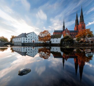 Jenseits einer Wasserfläche liegt rechts die Kathedrale von Uppsala und links das Kreismuseum.