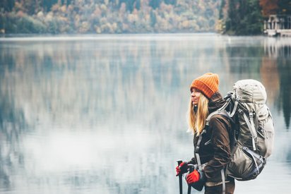 Die Finnische Seenplatte, ein Eldorado für Wanderer Vor einer glatten Wasserfläche, hinter der sich ein verschneiter Wald erstreckt, steht eine winterlich gekleidete Wanderin.