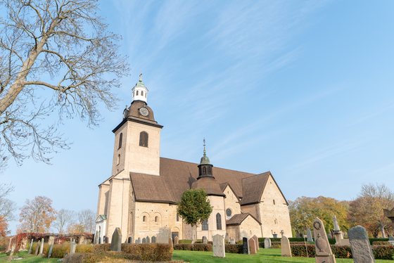 Kirche des Vreta-Klosterkomplexes Zu sehen ist eine alte Kirche umgeben von Grabsteinen, darüber erhebt sich ein leuchtend blauer Himmel.