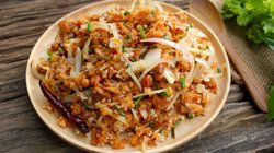 Ein Teller mit Naem Khao Tod, einem traditionellen laotischen Gericht aus knusprigem Reis, serviert mit frischen Kräutern, Limettenscheiben und Chilis, arrangiert auf einem Holztisch.