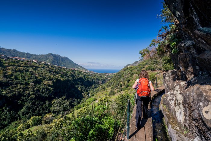 Frau in den Bergen auf einem ausgebauten Wanderpfad an einer Bergabhang neben einer Wasserstraße