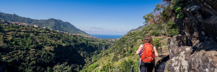 Wandertour entlang der Levada do Castelejo auf Madeira Frau in den Bergen auf einem ausgebauten Wanderpfad an einer Bergabhang neben einer Wasserstraße
